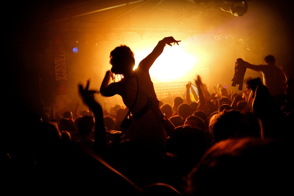 A woman dancing in a dark club with people around her and hands in the air