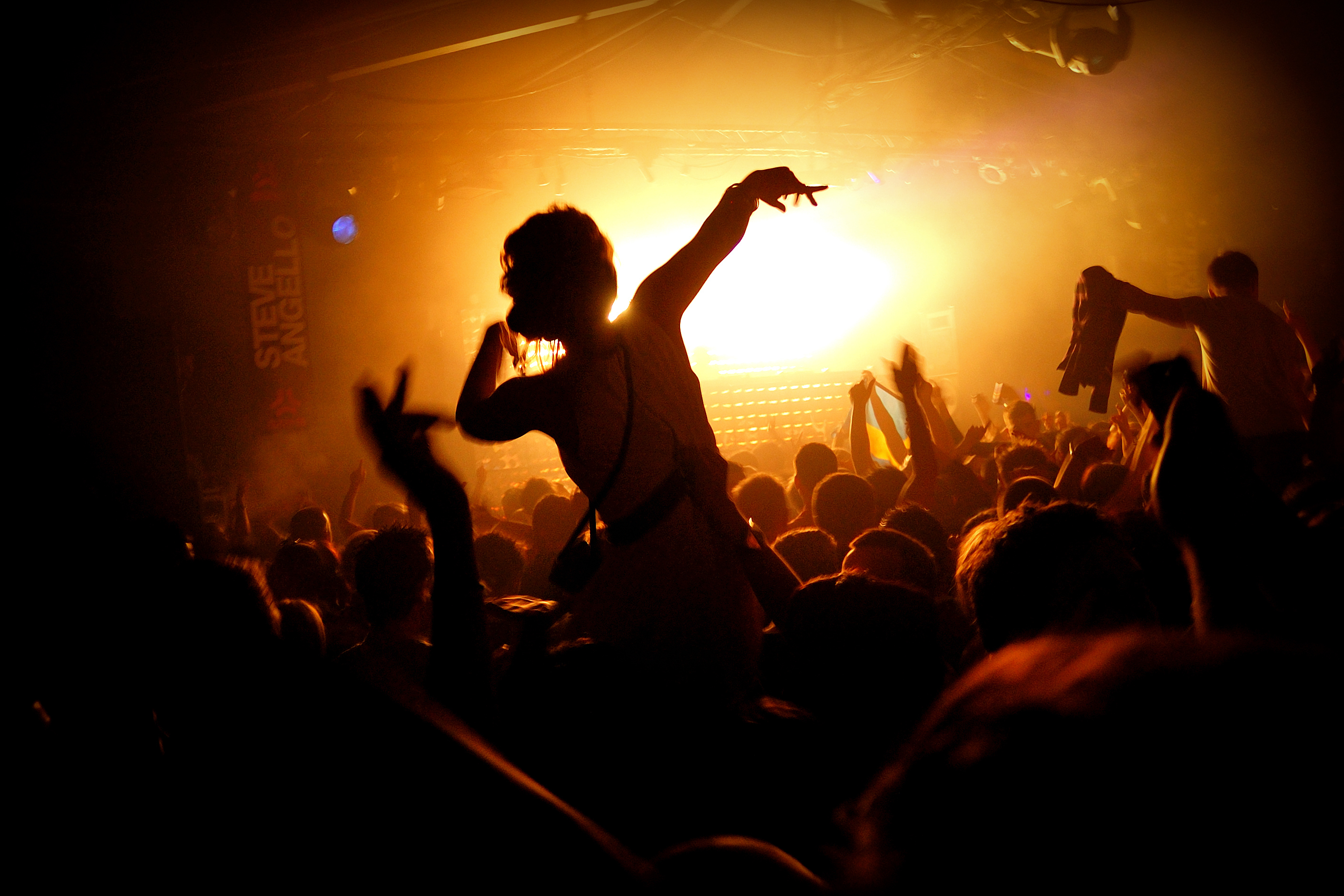 A woman dancing in a dark club with people around her and hands in the air